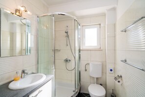 A modern bathroom with a glass-enclosed shower, a white sink, and a toilet.