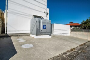 A building with a white facade, a metal structure with a blue sign, and a clear blue sky. - Marestella Zanpa (Nakagami-gun)