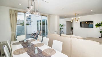Una sala moderna con un sofá, una mesa de comedor con individuales y un televisor montado en la pared.