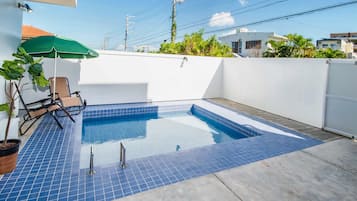 Una piscina en la azotea con baldosas azules, una sombrilla verde y una silla.