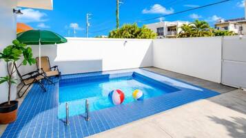Una piscina con dos pelotas de playa, una planta en maceta y una silla.