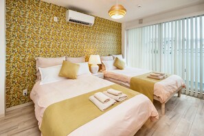 A hotel room with two beds, a patterned wallpaper, a ceiling fan, and a view of the outside.