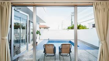 A sliding glass door leading to a balcony with a pool and two chairs.