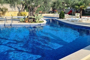 Ein Swimmingpool mit einer gefliesten Kante, umgeben von Liegestühlen und Topfpflanzen.