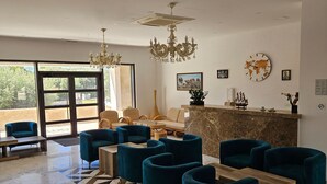 Un vestíbulo de hotel con una recepción, área de estar con sillas, una araña y un gran ventanal.