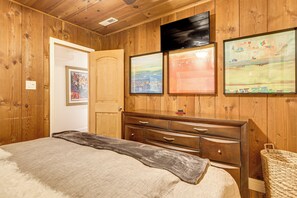 Ein Zimmer mit Holzwänden, einem Bett, einer Kommode und drei gerahmten Kunstwerken an der Wand.