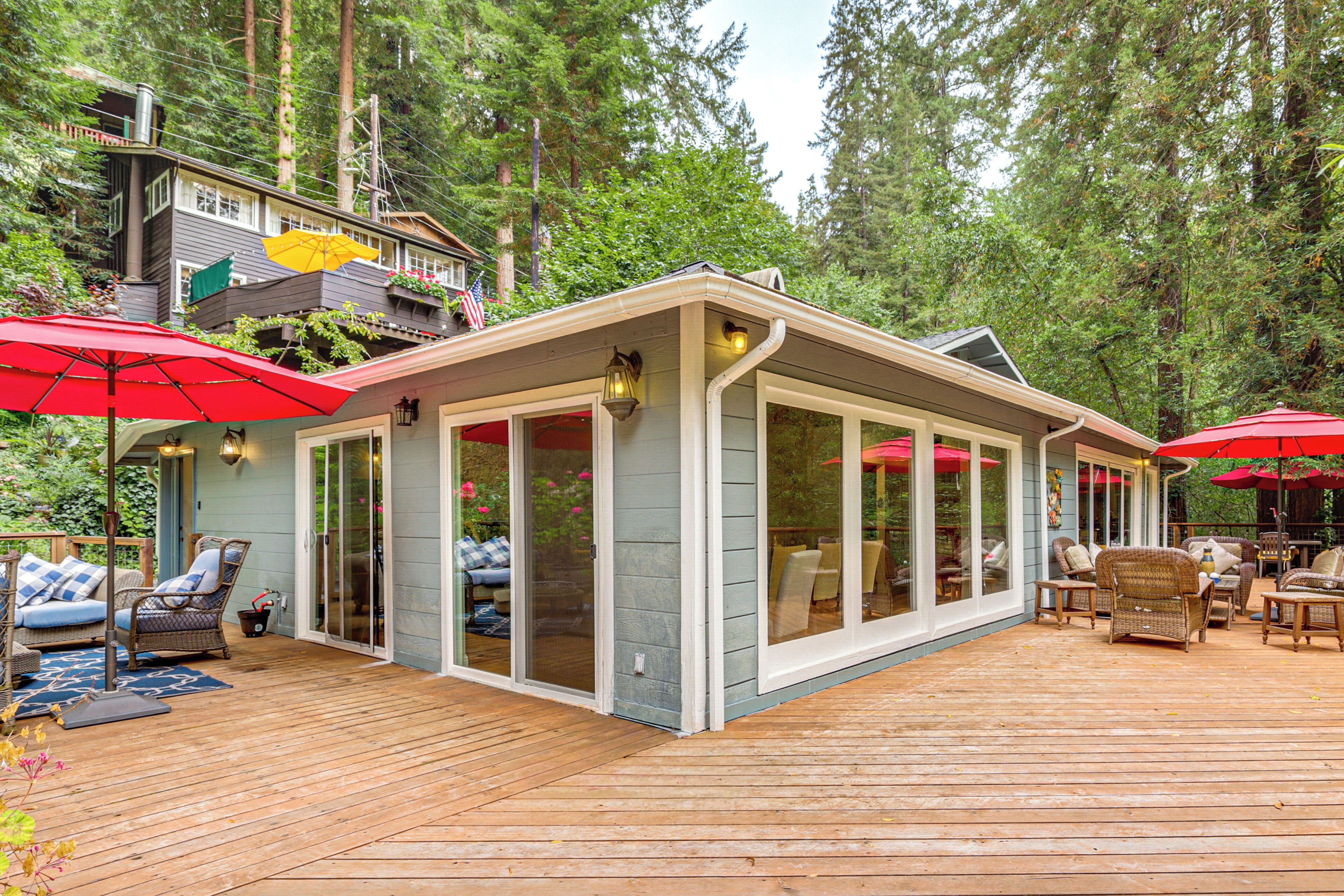 A covered outdoor deck with a dining area, furnished with wicker chairs and red umbrellas.