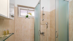 Un bany amb una cabina de dutxa de vidre, un braç de dutxa manual, un seient de dutxa de vidre i una finestra amb una planta d'orquídea.