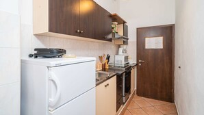 Cuina compacta amb rentadora blanca, microones i fogó. Hi ha un armari de fusta sobre l'aigüera i una porta amb un cartell.