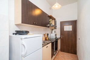 Eine kompakte Küche mit einer weißen Waschmaschine, einer Mikrowelle und einem Herd. Oberhalb der Spüle befindet sich ein Holzschrank und eine Tür mit einem Hinweisschild.