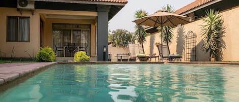 A swimming pool with lounge chairs and umbrellas, surrounded by buildings with tiled roofs.