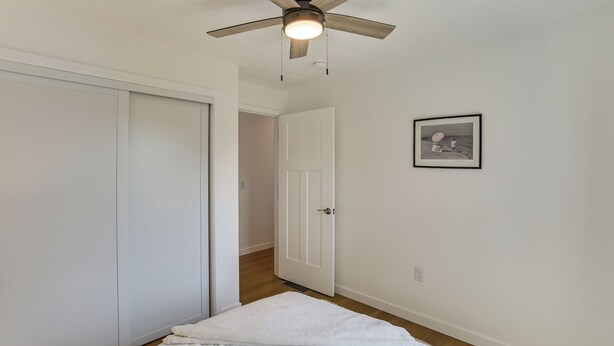 Un dormitorio con cama, ventilador de techo, una puerta y un cuadro en la pared.