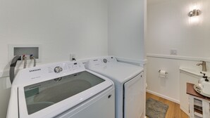 Lavandería con dos lavadoras y secadoras Samsung blancas de autolimpieza, un ventanal pequeño y un lavabo con dispensador de toallas.