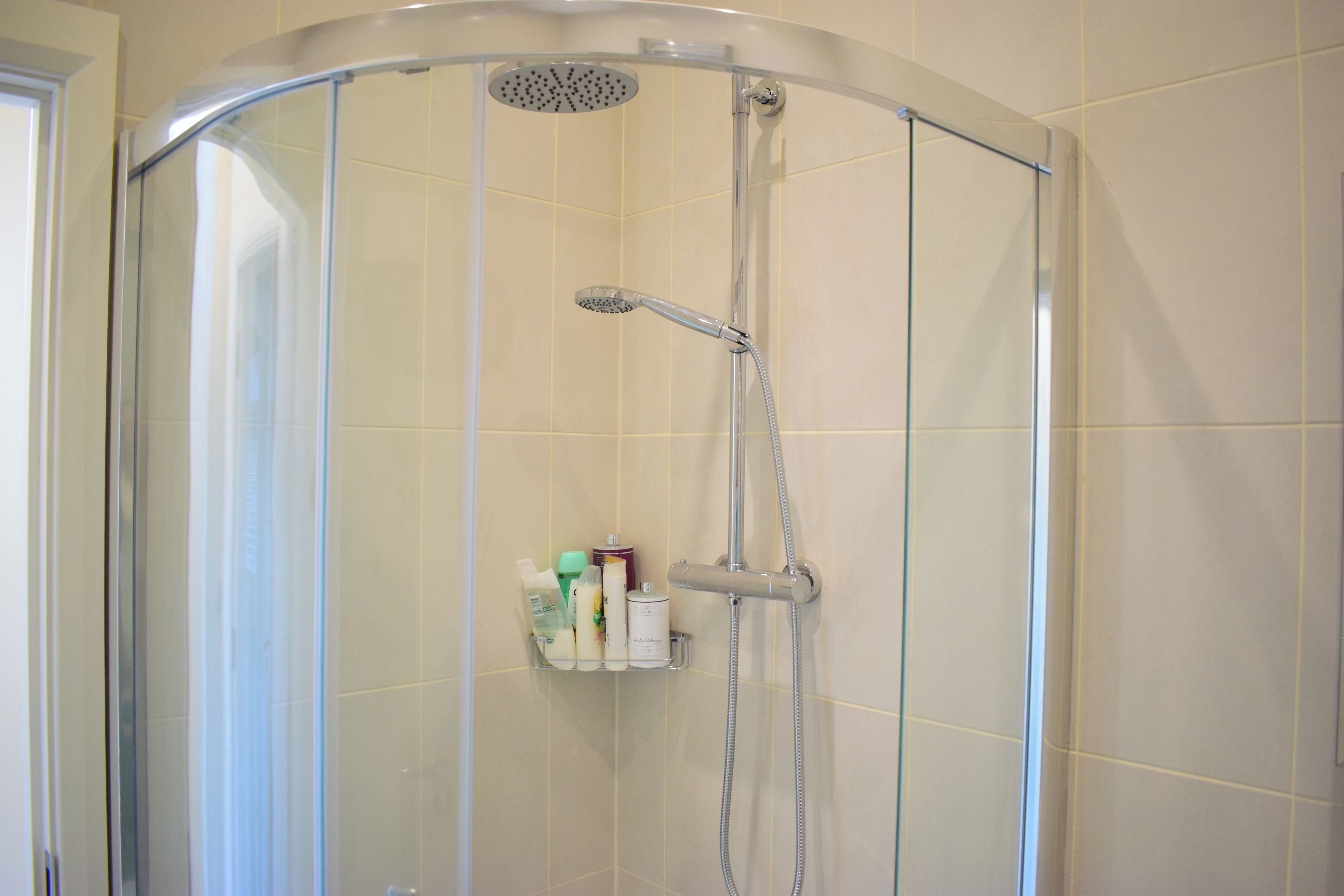 Un box de ducha con puerta de vidrio, un cabezal de ducha de mano y un grifo empotrado.