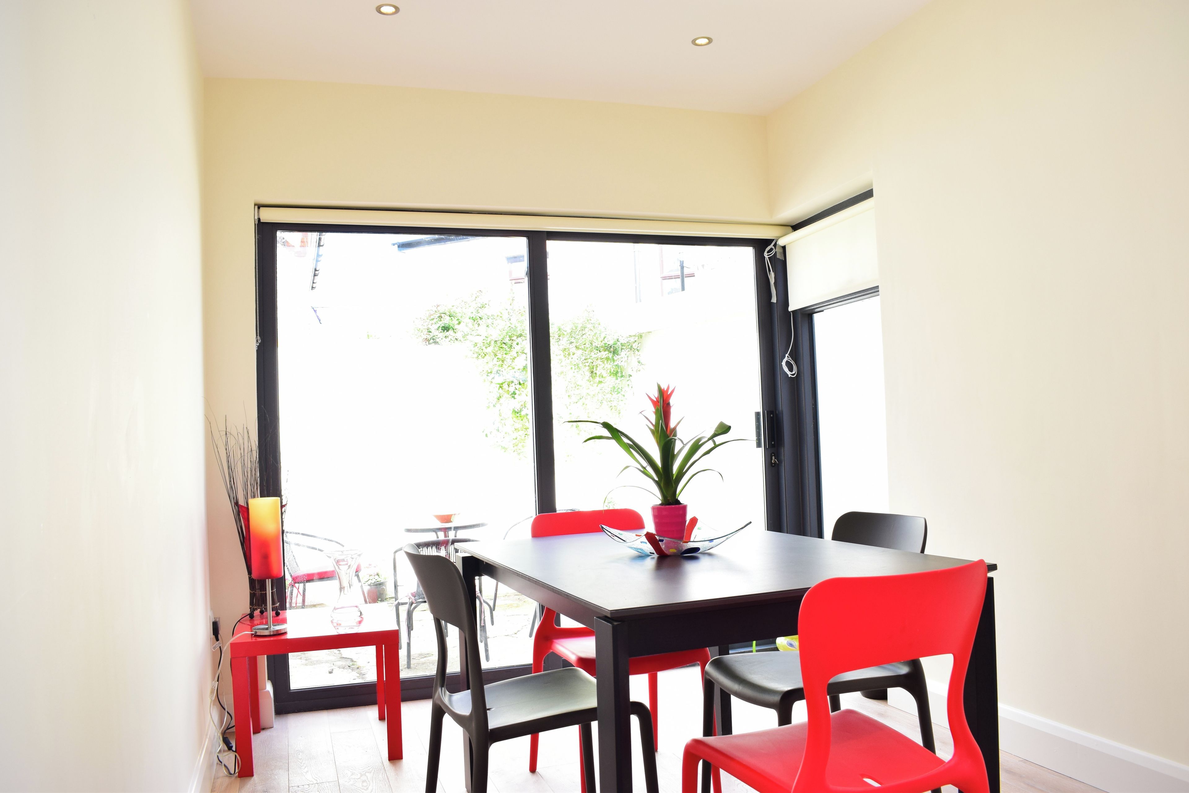 A dining area with a table and chairs, a potted plant, and a view through a large window.