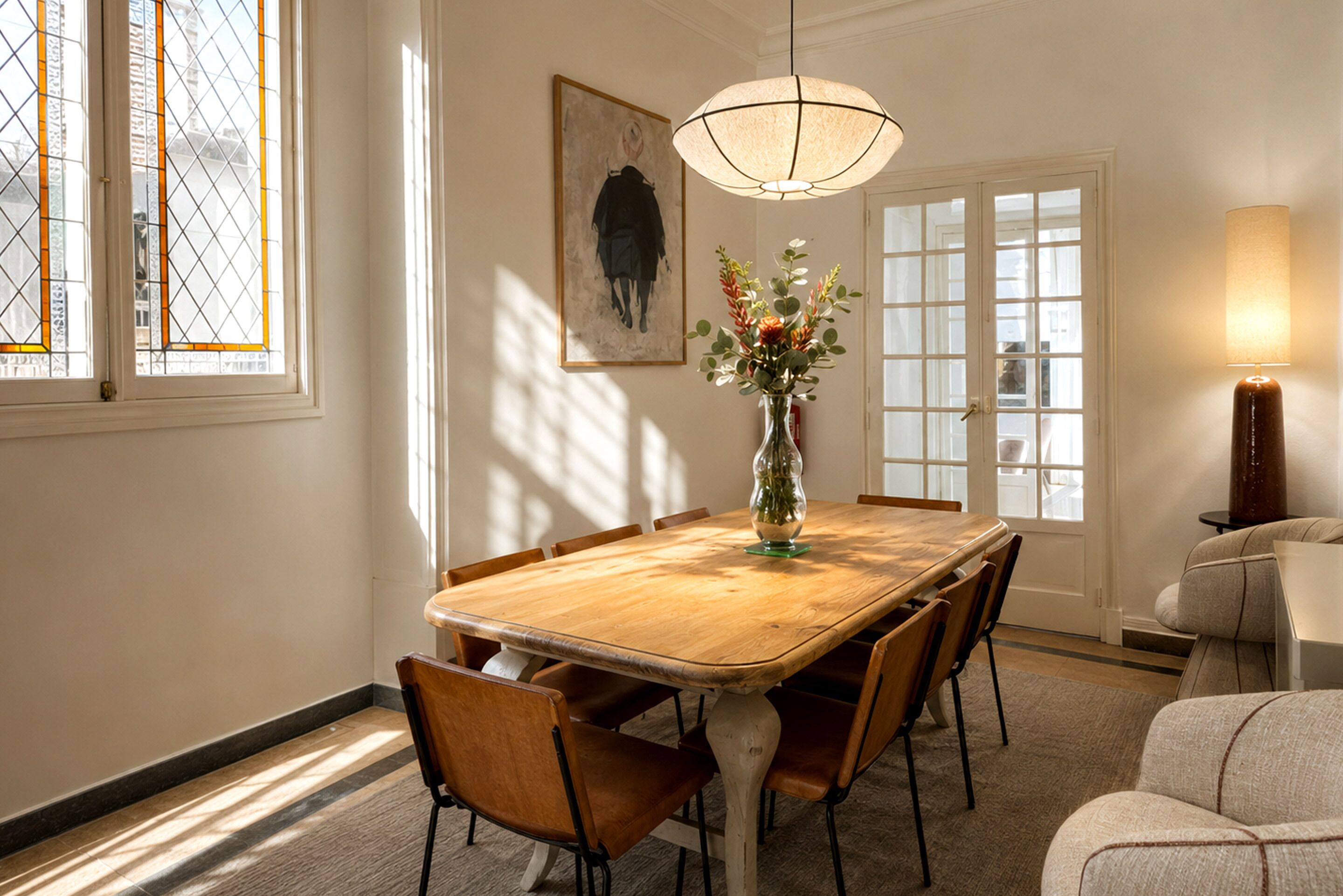 Comedor con una mesa de madera, sillas, un jarrón con flores, un cuadro en la pared y una ventana con vistas.