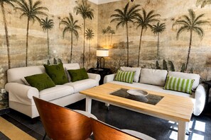 A living room with two white sofas, green and striped pillows, a wooden coffee table, and a wall mural of palm trees. - Genteel Home Bartolomé de Medina (Seville)