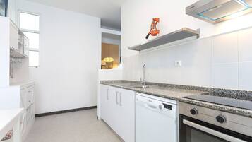 Una cuina moderna amb armaris blancs, taulell de granat, rentaplats, forn i campana extractora integrats.