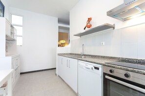 Una cocina moderna con armarios blancos, encimera de granito, lavavajillas, horno y campana extractora integrada.