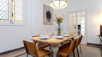 Un comedor con una mesa de madera dispuesta para seis personas, rodeada de seis sillas, un jarrón con flores y un cuadro en la pared.