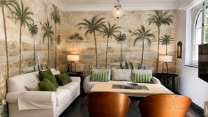 Una habitación con un sofá, dos sillones, una mesita de centro y un mural en la pared con palmeras.