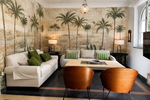 Una habitación con un sofá, dos sillones, una mesita de centro y un mural en la pared con palmeras.