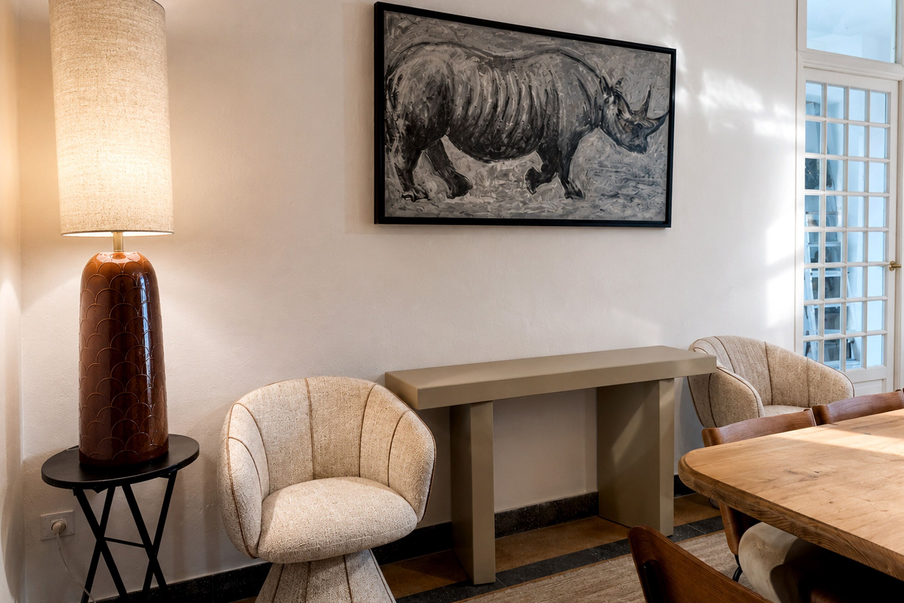 Una habitación con una mesa, sillas, una lámpara y un cuadro con la imagen de un rinoceronte.