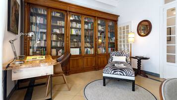 A room with a wooden bookcase, a desk with a lamp, a zebra-patterned chair, and a round table with a lamp.