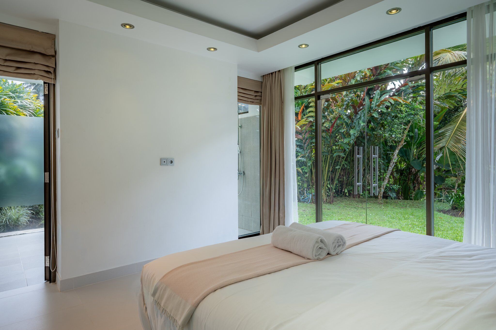 Un dormitorio moderno con una cama grande, ducha y vistas a un jardín exuberante a través de ventanales de gran altura.