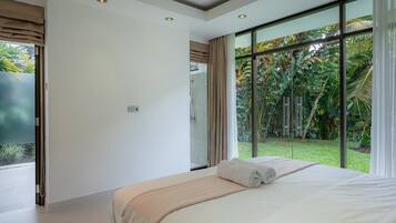 Un dormitorio moderno con una cama grande, ducha y vistas a un jardín exuberante a través de ventanales de gran altura.