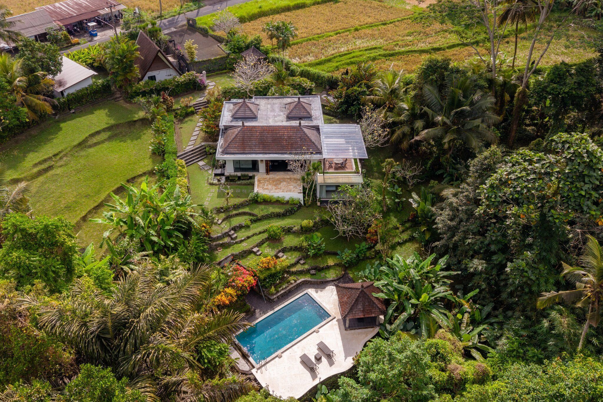 A large house with a swimming pool, surrounded by lush greenery and terraced fields.