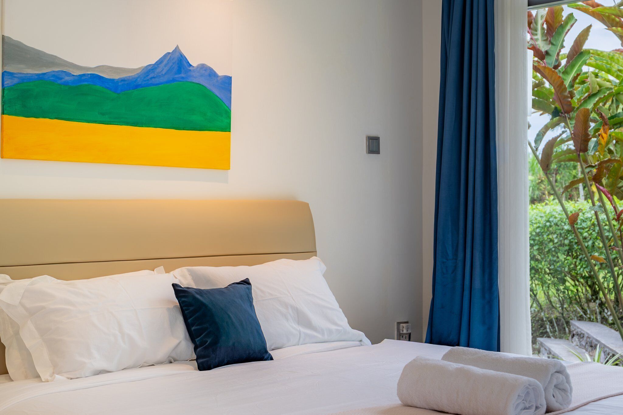 Une chambre d’hôtel avec un lit, des oreillers, un tableau et une vue sur la verdure par la fenêtre.
