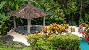Un kiosque doté d’un toit en tuiles, entouré d’une végétation luxuriante et d’une piscine.