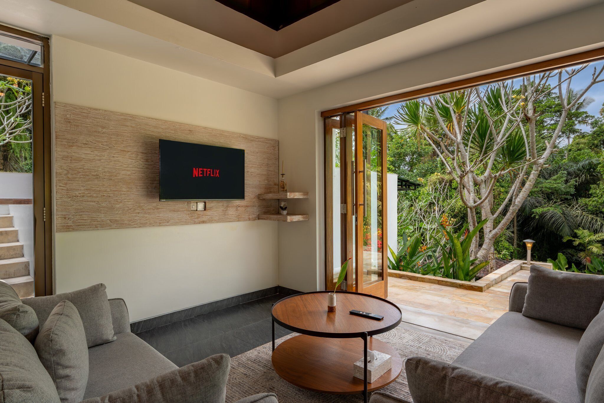 Una sala de estar moderna con un televisor de pantalla plana montado en una pared de madera, una mesa de centro redonda y sofás grises.