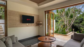 Una sala de estar moderna con un televisor de pantalla plana montado en una pared de madera, una mesa de centro redonda y sofás grises.