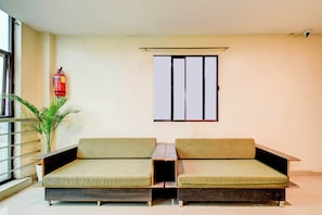 A room with two green cushioned sofas, a small table, a potted plant, a fire extinguisher, and a window with a metal frame. - Super Collection O Abids Hyderabad (Hyderabad)