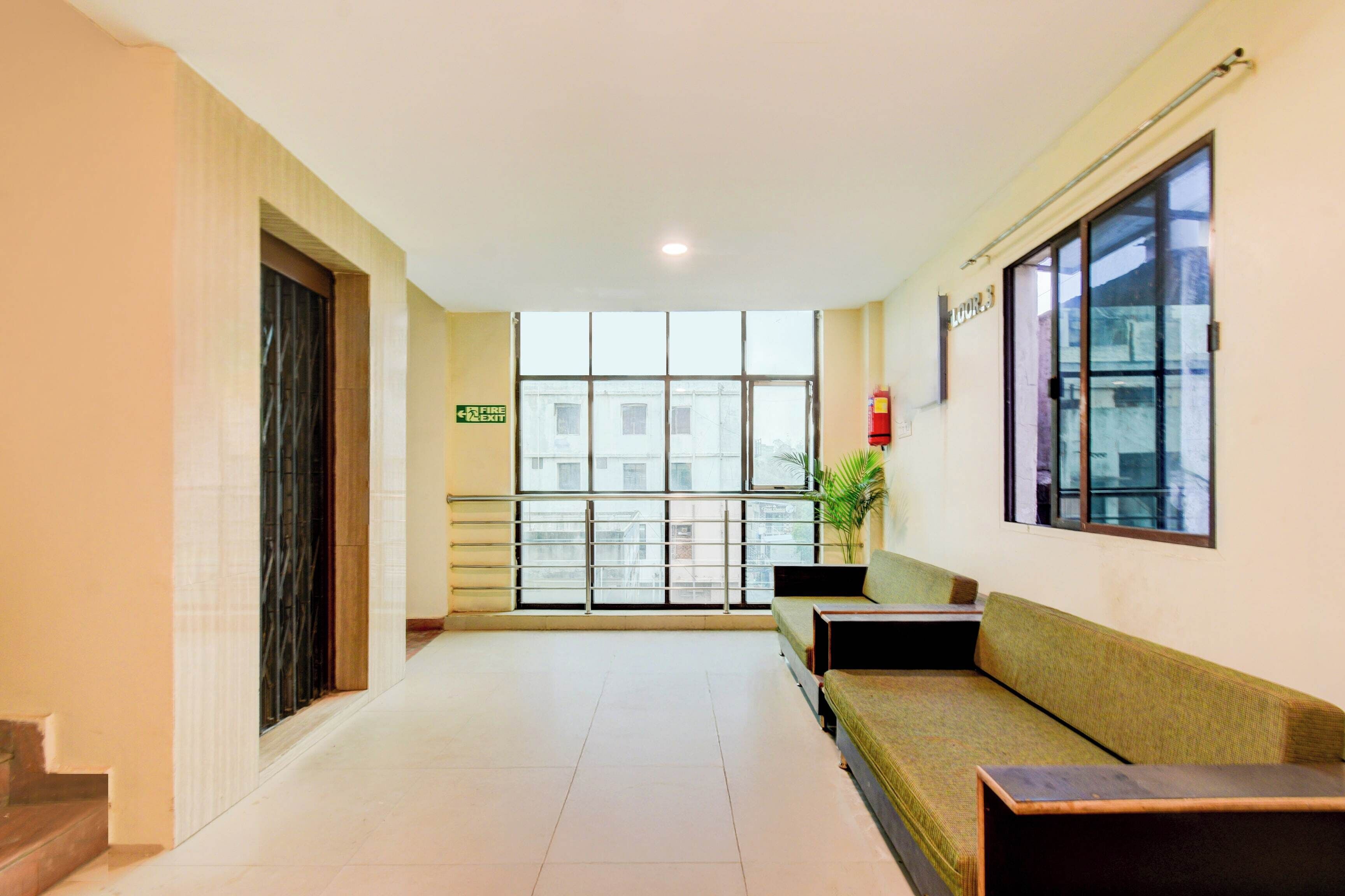 A hotel lobby with a reception desk, a seating area, a fire exit sign, and a large window with a view of buildings outside.