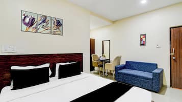 Habitación de hotel con cama, un sofá azul, una mesa de comedor con sillas y obras de arte en la pared.