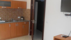 A kitchen with wooden cabinets, a sink, and a kettle. There is a door leading to another room. - Apartments Lux Lukić Utjeha - One bedroom apartment (Utjeha)
