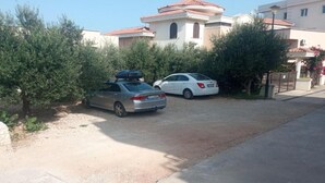 A residential area with two parked cars, a building with a red-tiled roof, and a clear sky. - Apartments Lux Lukić Utjeha - One bedroom apartment (Utjeha)