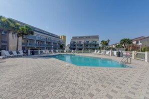 Una piscina con sillas de descanso y un edificio con varios balcones al fondo.