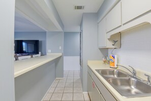 Cocina estrecha con un lavamanos, un televisor al fondo y un inodoro visible al final del pasillo.