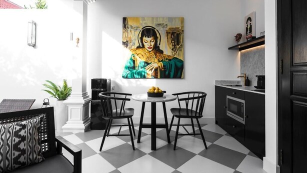 A modern kitchen with a checkered floor, a dining table with chairs, a painting on the wall, and a black cabinet with a microwave. - Martini Beachside 2 (Canggu)