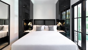 A large bed with white bedding, flanked by dark wooden cabinets and nightstands with decorative items. - Martini Beachside 2 (Canggu)