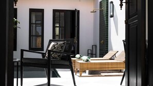 A room with a black chair, a wicker sofa, and a large window with black shutters. - Martini Beachside 2 (Canggu)
