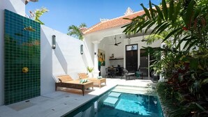 A poolside area with a lounge chair, a dining table, and a ceiling fan. - Martini Beachside 2 (Canggu)