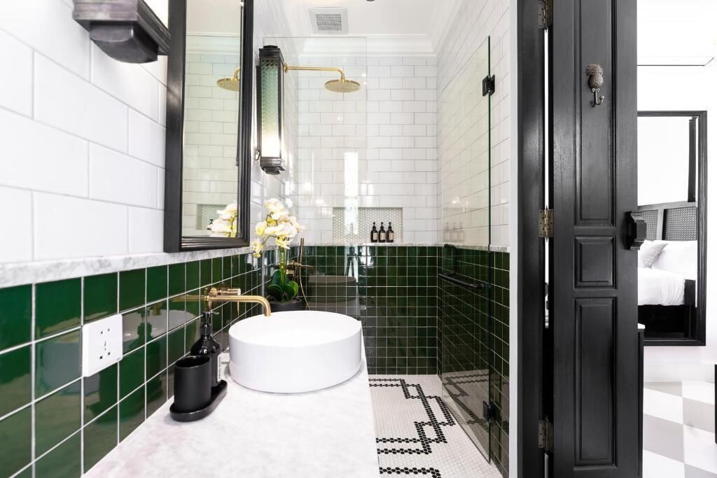 A modern bathroom with a round sink, a shower with a gold fixture, and a black door.