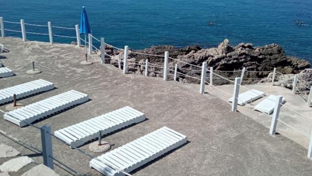 A beachside area with white lounge chairs and a rocky shoreline. - Apartments Lux Lukić Utjeha - One bedroom apartment (Utjeha)