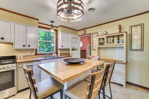 A kitchen with a central island, white cabinetry, a built-in oven, and a dining area with chairs. - Boating, Bonfires & Lake Views! Michigan Getaway (Ellsworth)