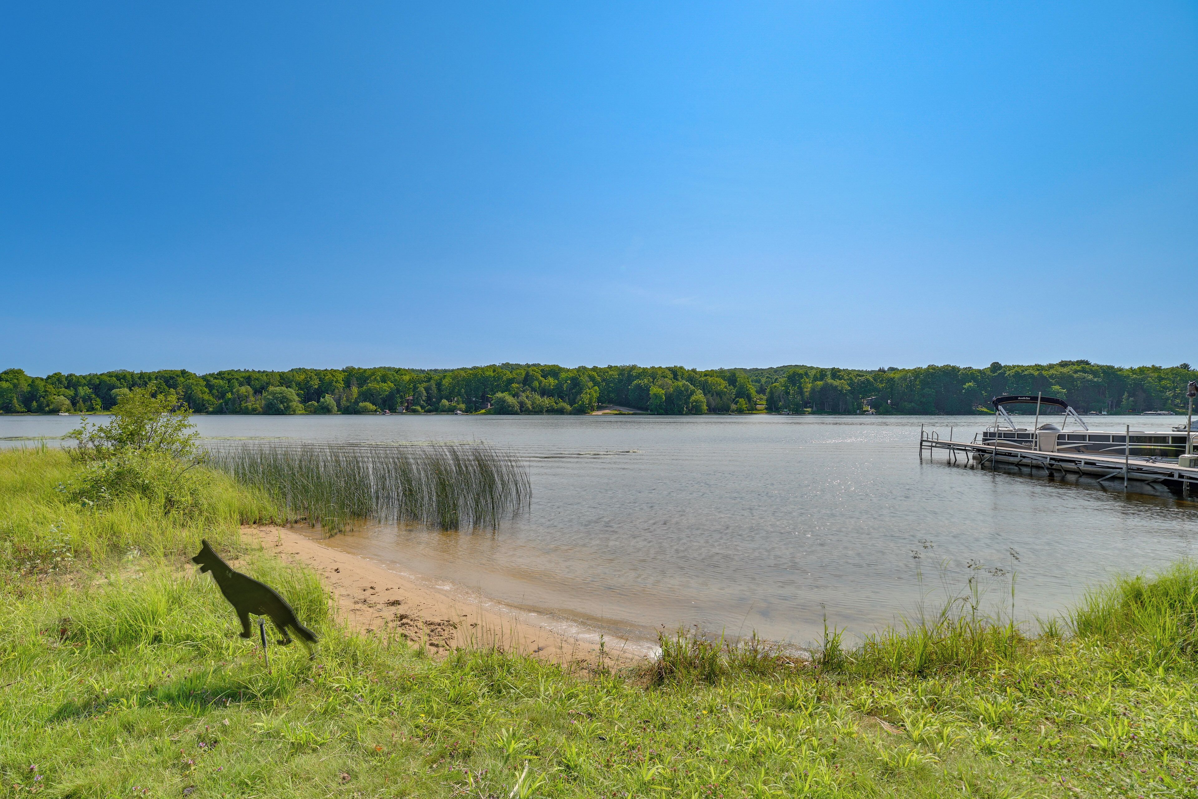 A lake with a dock and a grassy area with a dog.